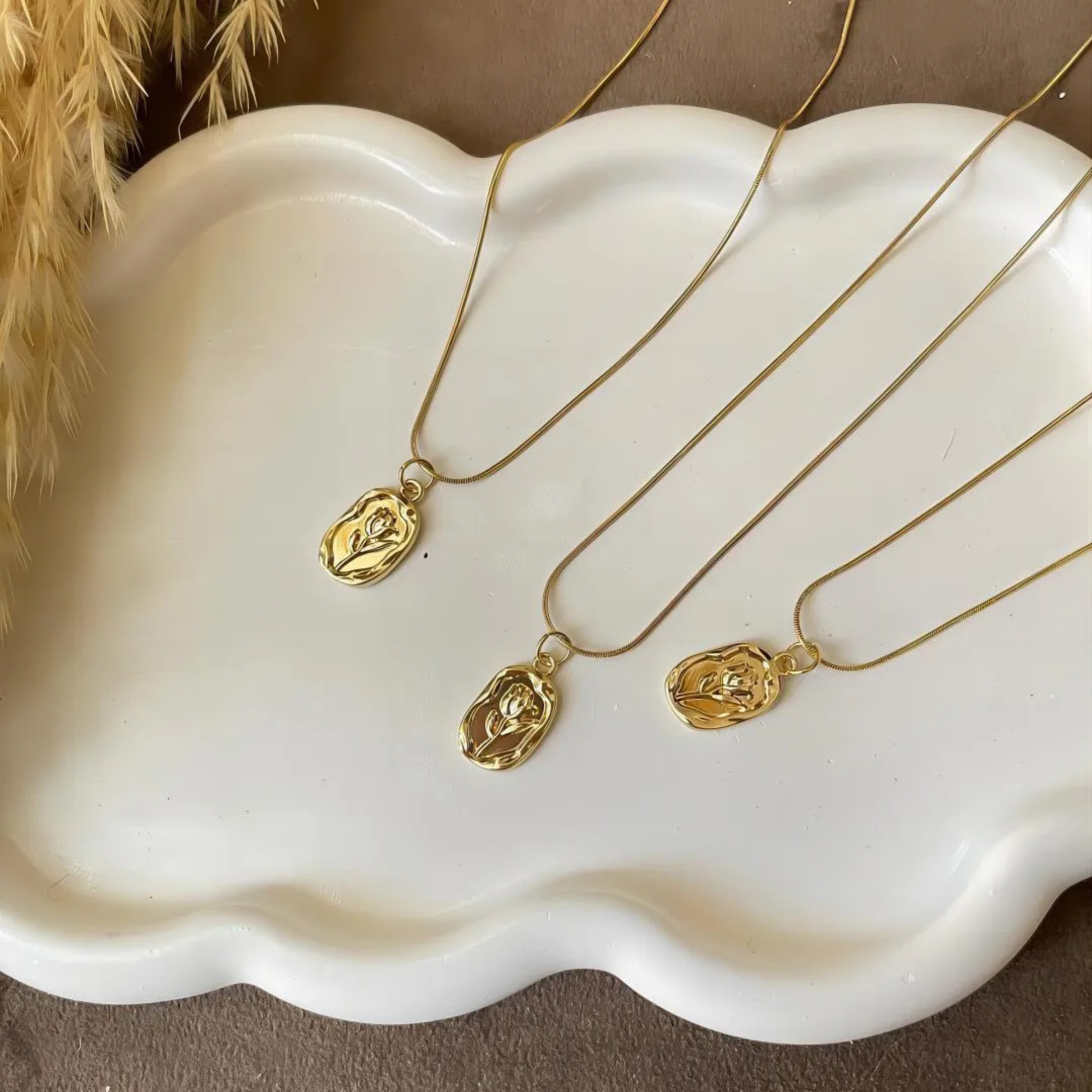 Three gold necklaces with pendants on a white scalloped tray.