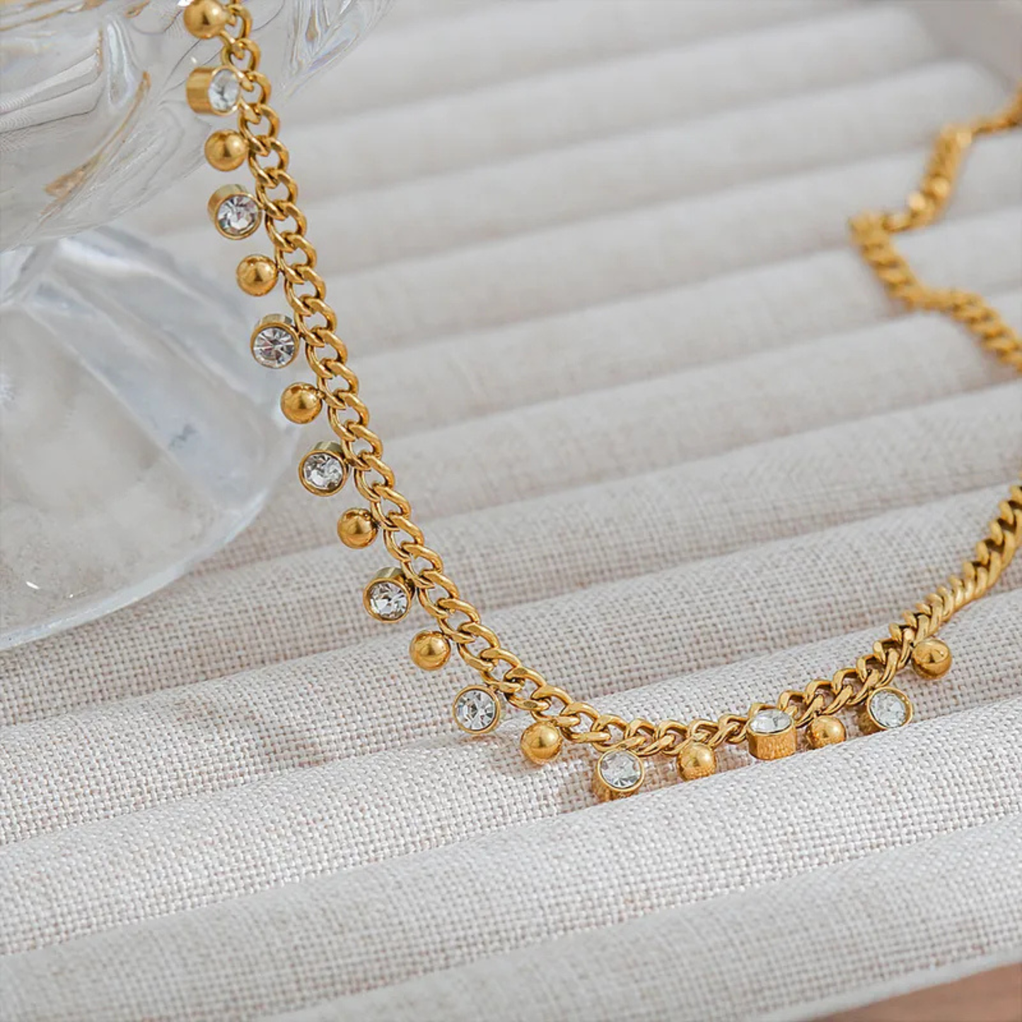 Gold necklace with small beads and crystals on a textured beige surface