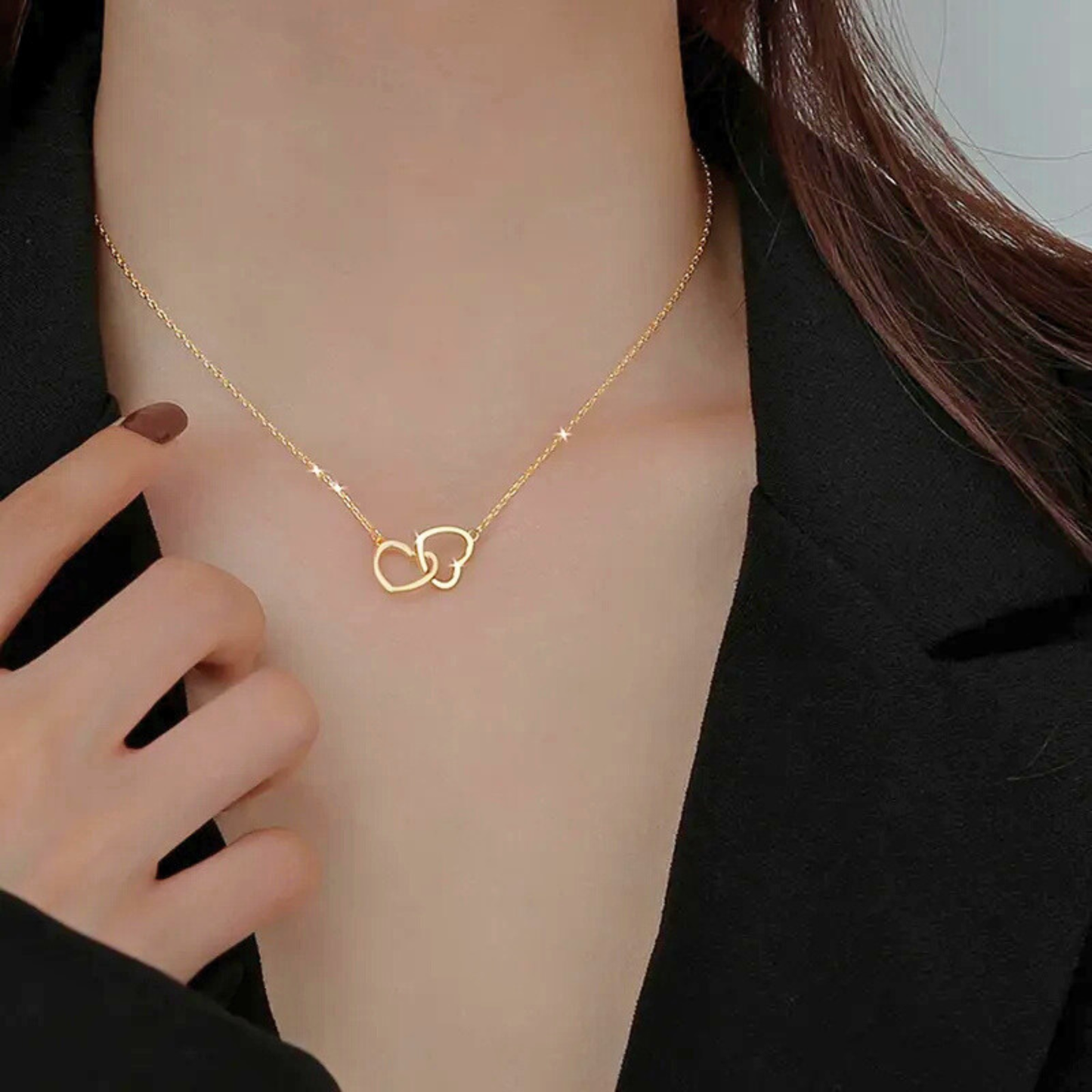 Gold necklace with interlocking heart pendants on a person wearing a black outfit.