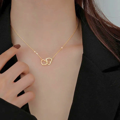 Gold necklace with interlocking heart pendants on a person wearing a black outfit.