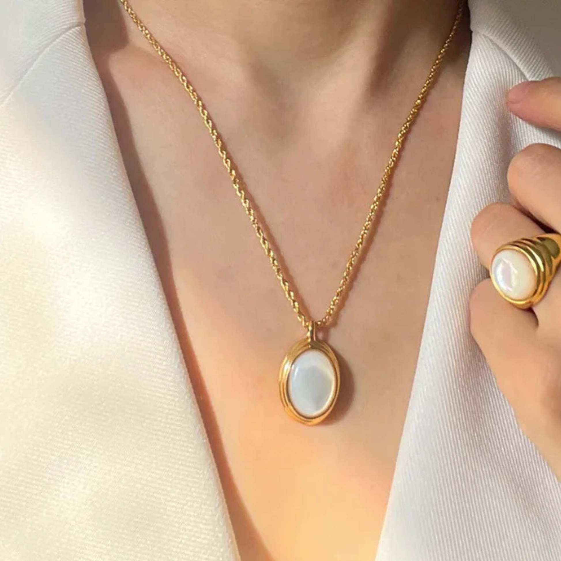 Gold necklace with a pendant and matching ring on a neutral background