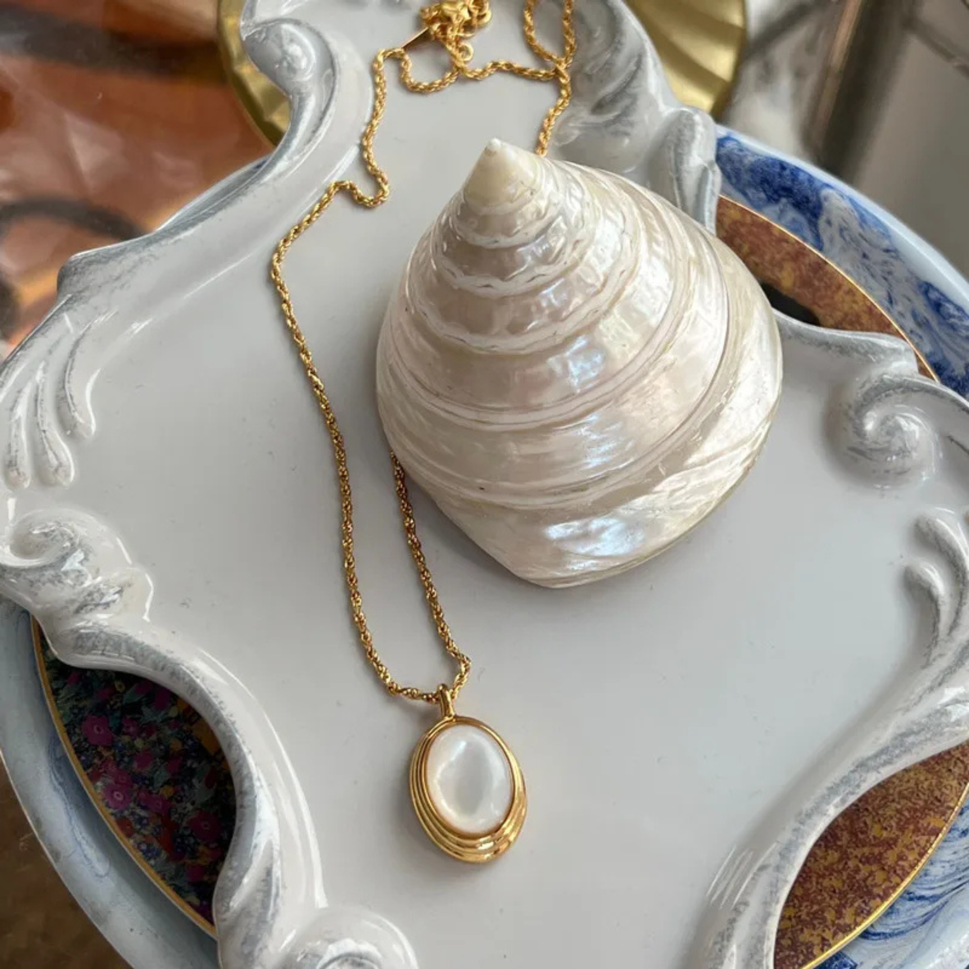 Gold necklace with a shell pendant on a decorative white dish
