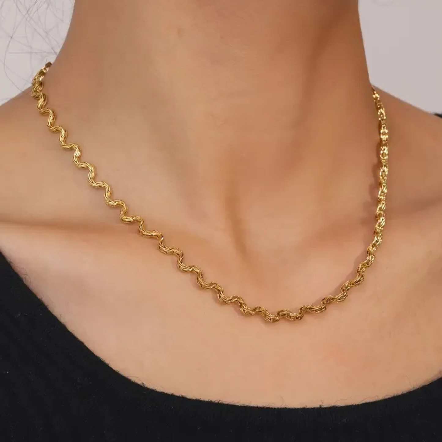 Gold chain necklace on a person wearing a black top against a neutral background