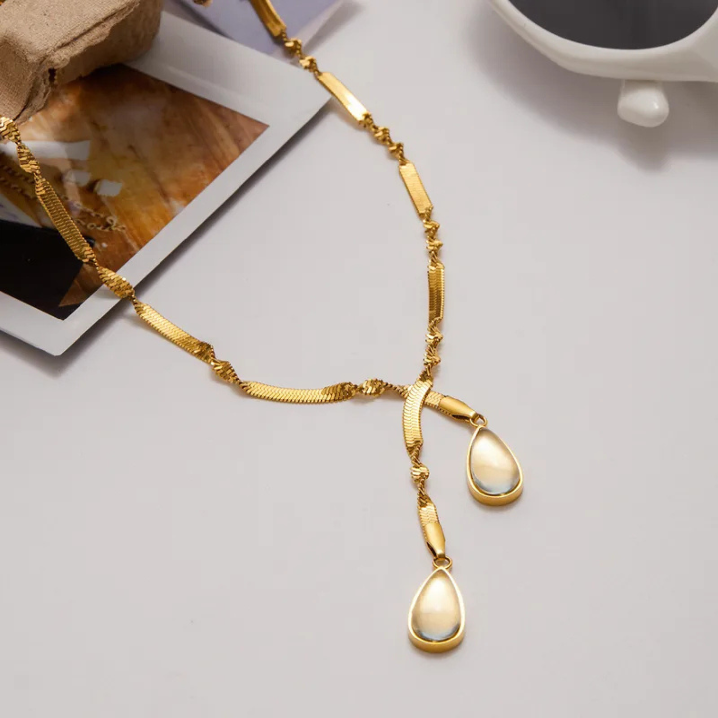 Gold necklace with teardrop pendants on a light gray surface