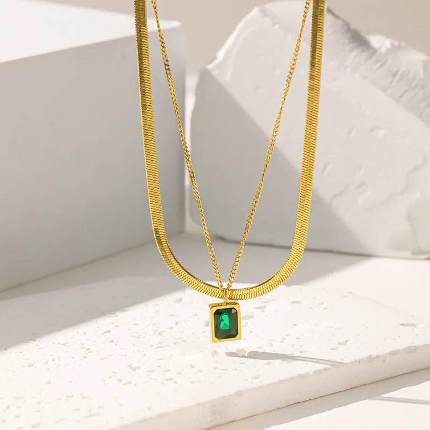 Gold necklaces with green gemstones on a white surface