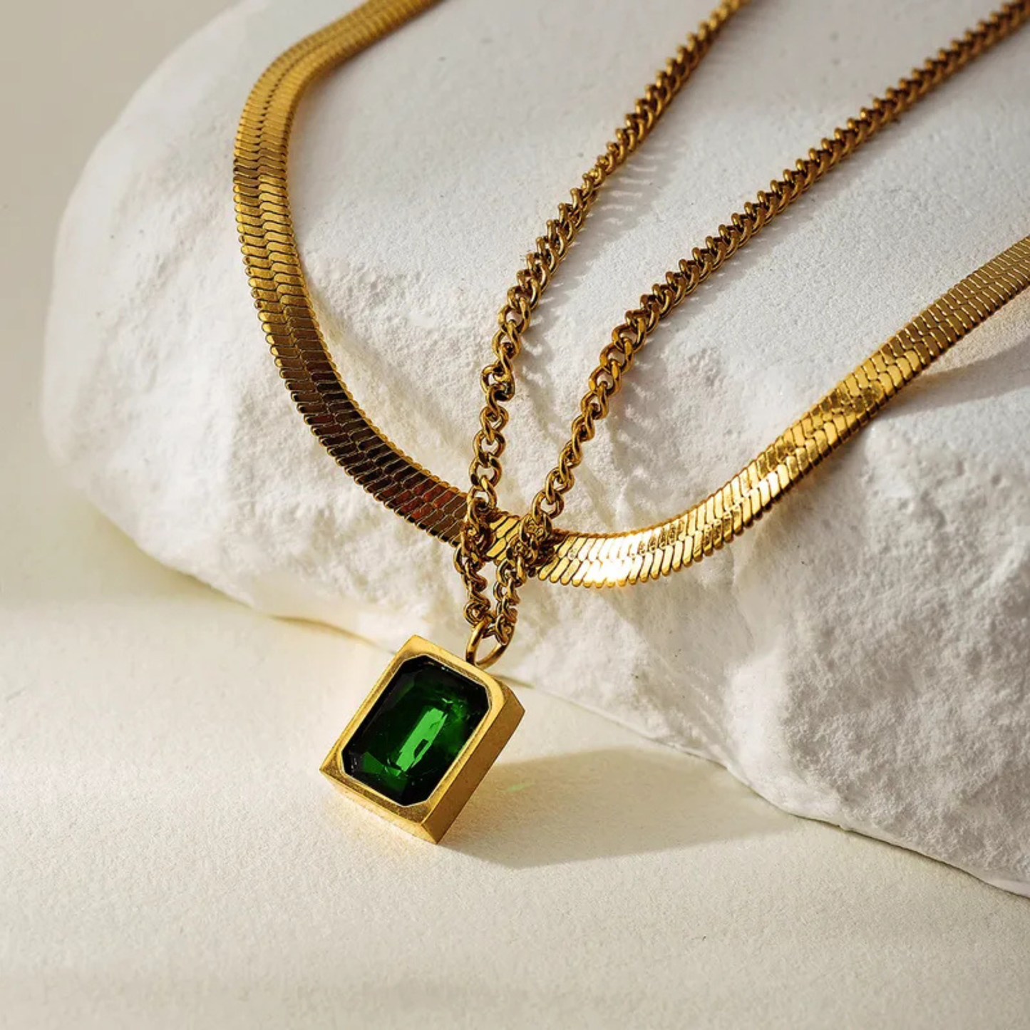 Gold necklace with a green gemstone pendant on a textured white surface