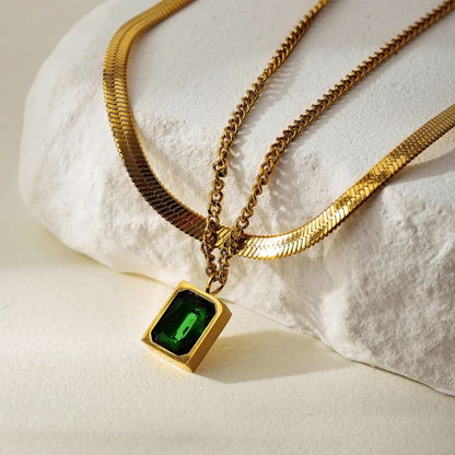 Gold necklace with a green gemstone pendant on a textured white surface