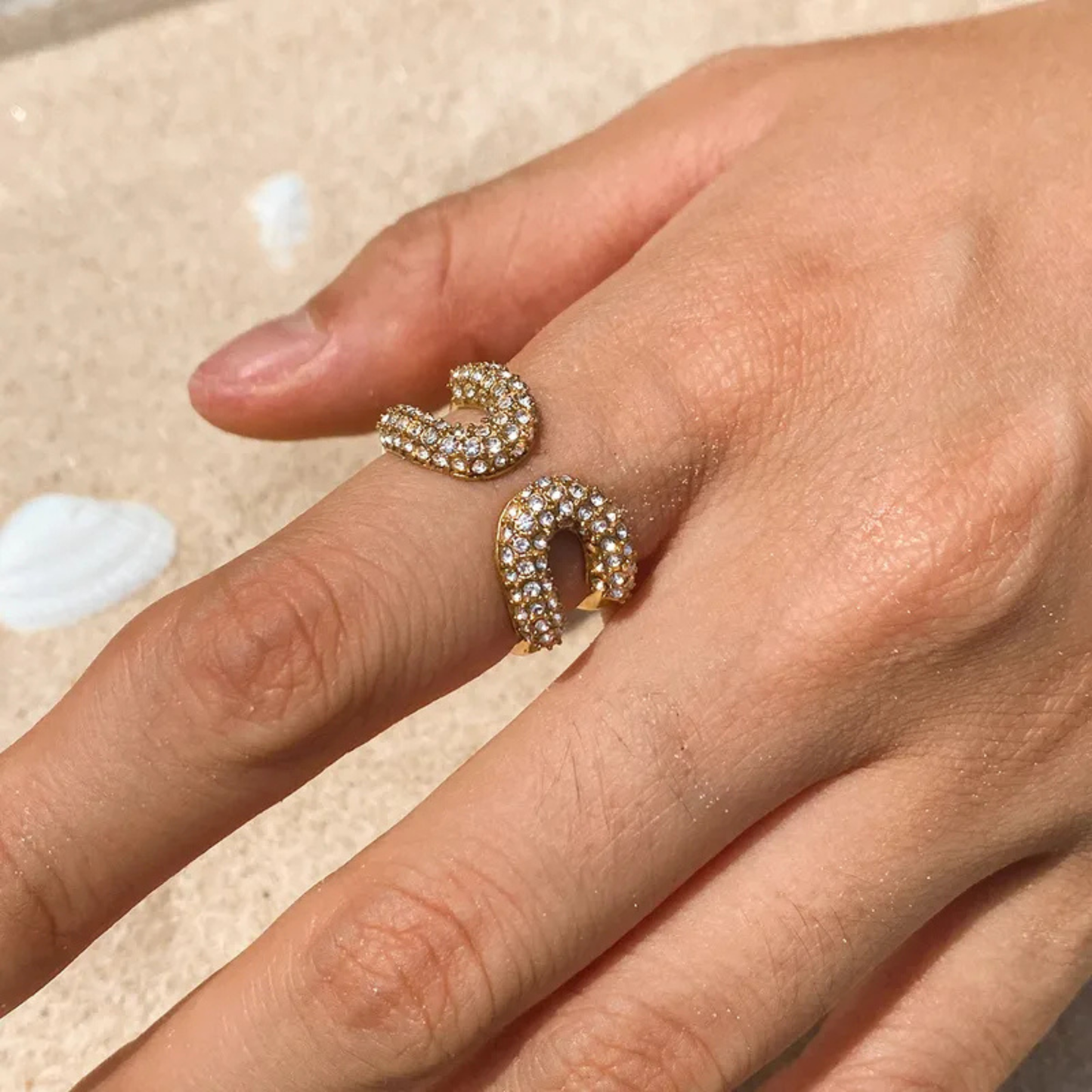 Hand wearing two gold rings with diamond accents on a light background