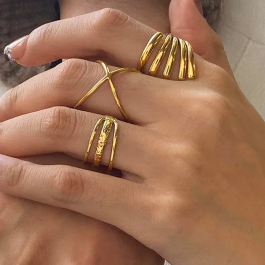 Close-up of a hand wearing three gold rings on a neutral background