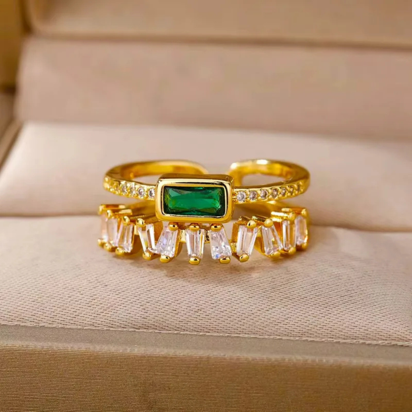 Gold ring with emerald and baguette diamonds on a beige fabric background