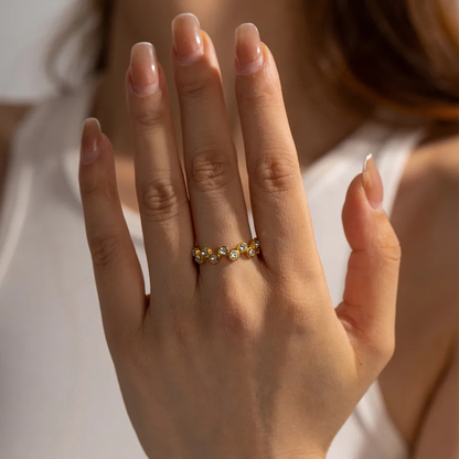 Close-up of a hand wearing a gold ring with small stones on a neutral background