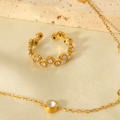 Gold ring with embedded stones and gold chain on a beige fabric background