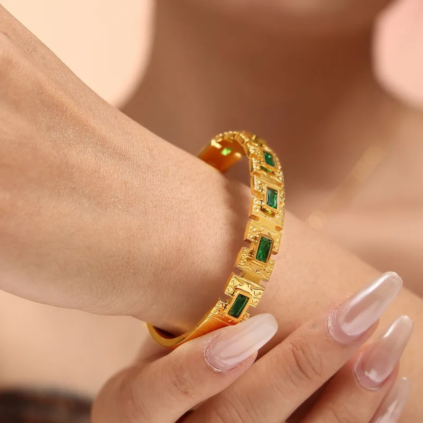 Gold bracelet with green gemstones on a wrist against a neutral background