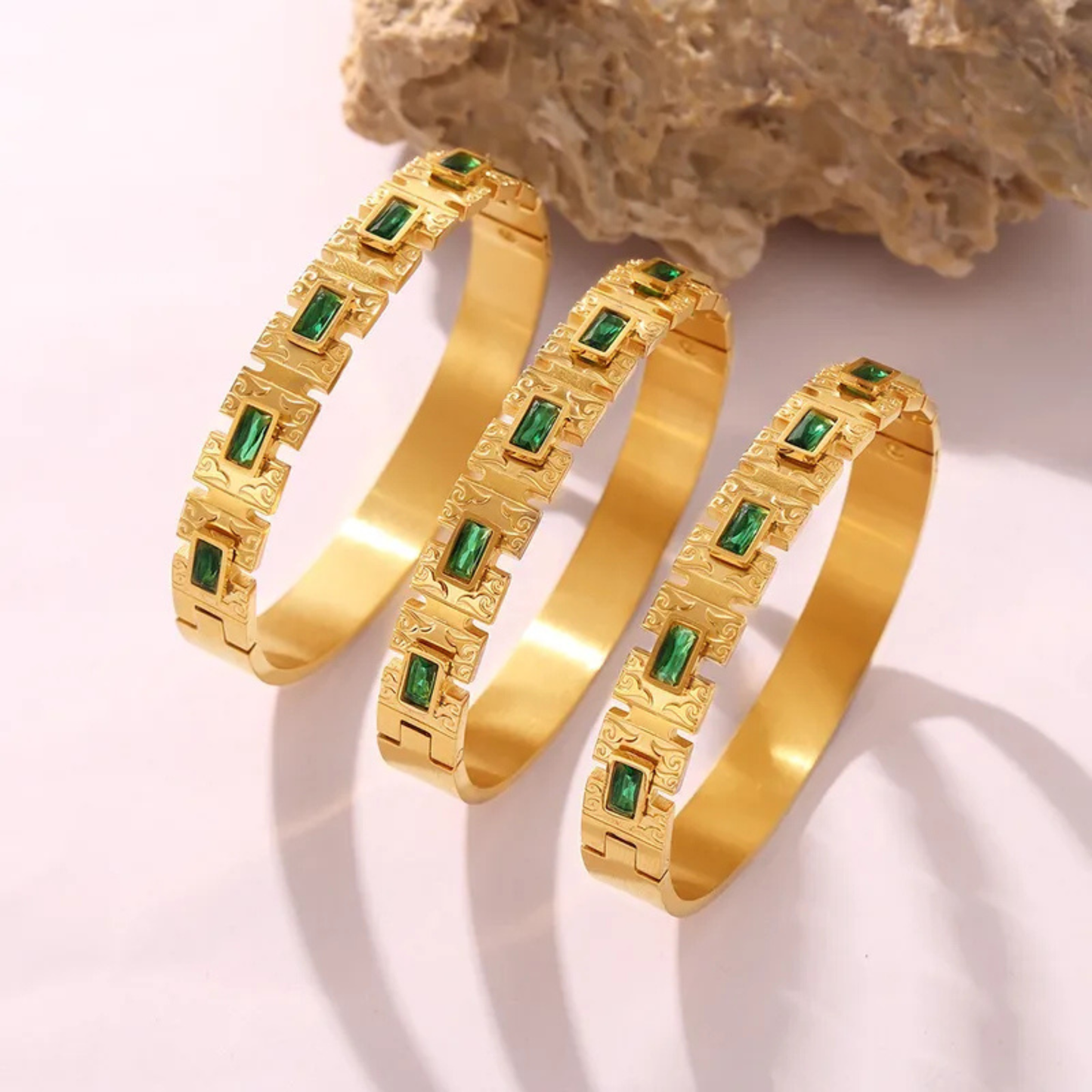 Three gold bangles with green gemstones on a light background