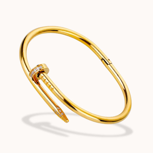 A gold-toned bar cuff bracelet with a small diamond-set accent, shown on a clean off-white background.