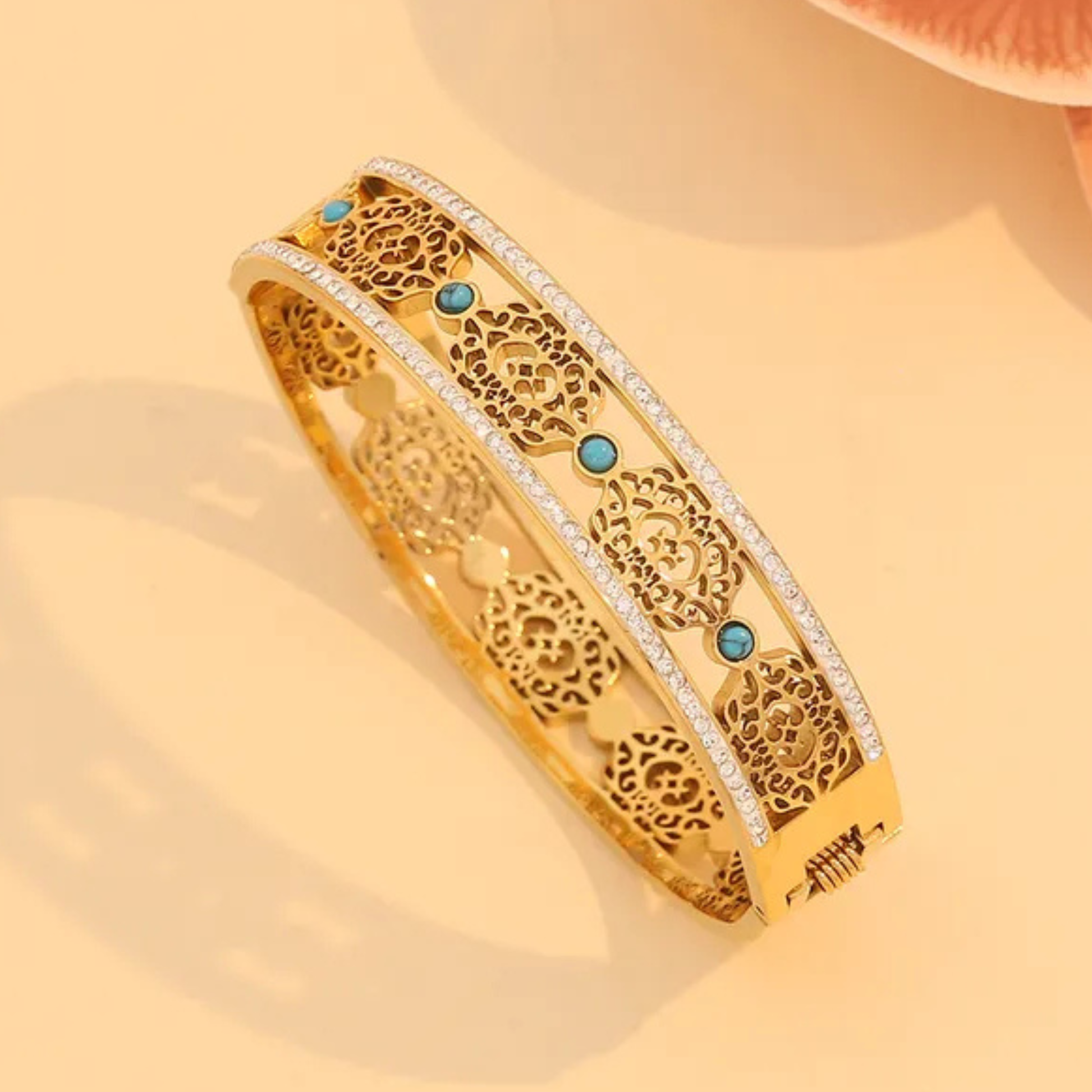 Gold bracelet with intricate design and blue stones on a beige background