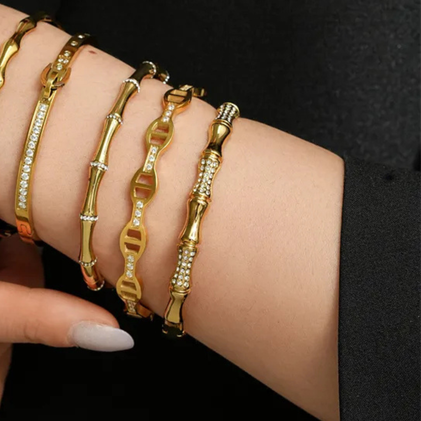 Gold bracelets on a wrist against a black background