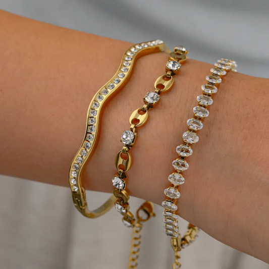 Gold and diamond-encrusted bracelets on a wrist against a neutral background
