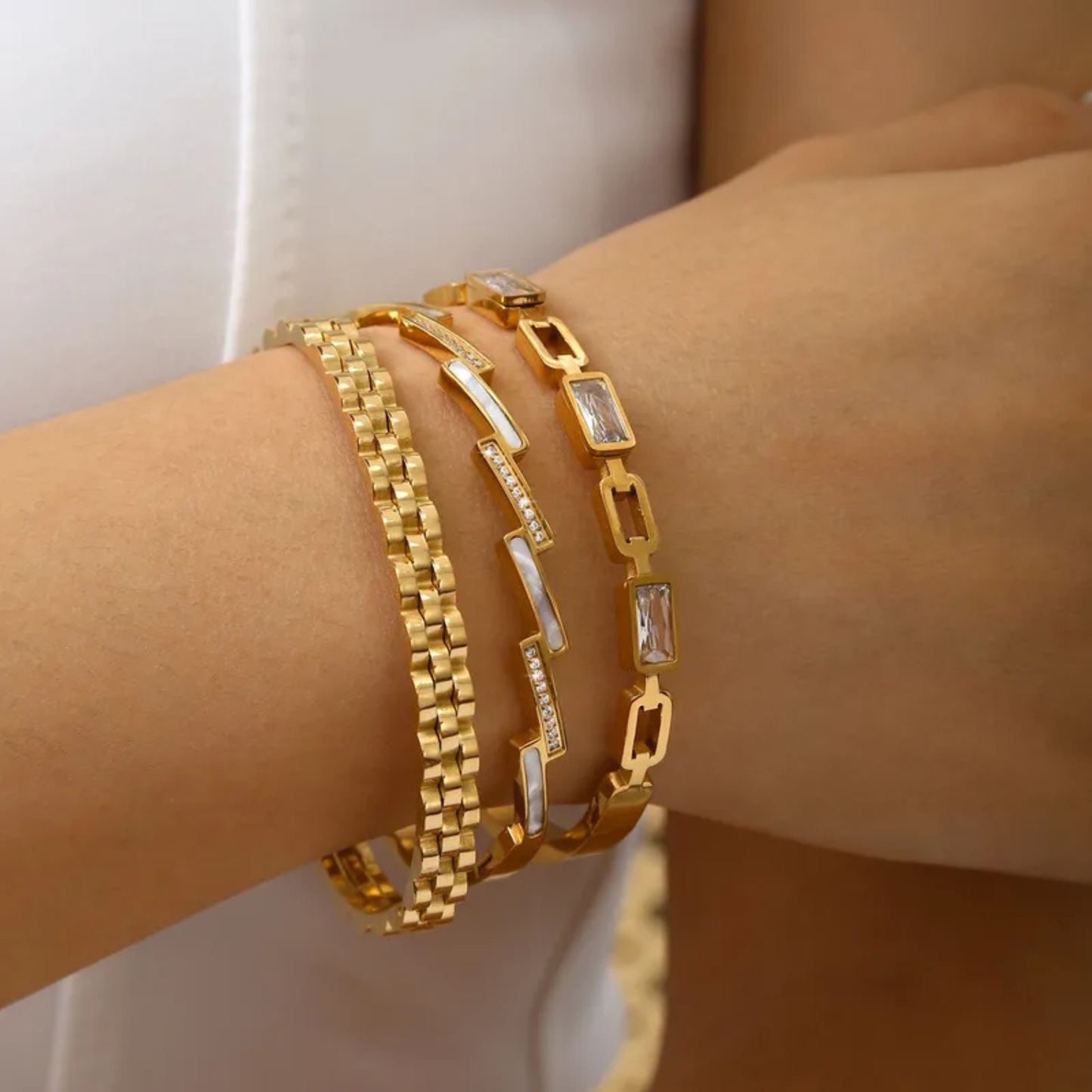 Gold bracelets on a wrist with a neutral background