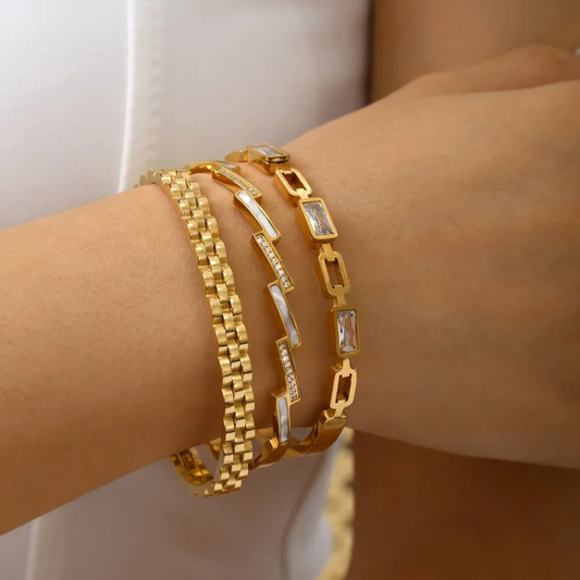 Gold bracelets on a wrist with a neutral background