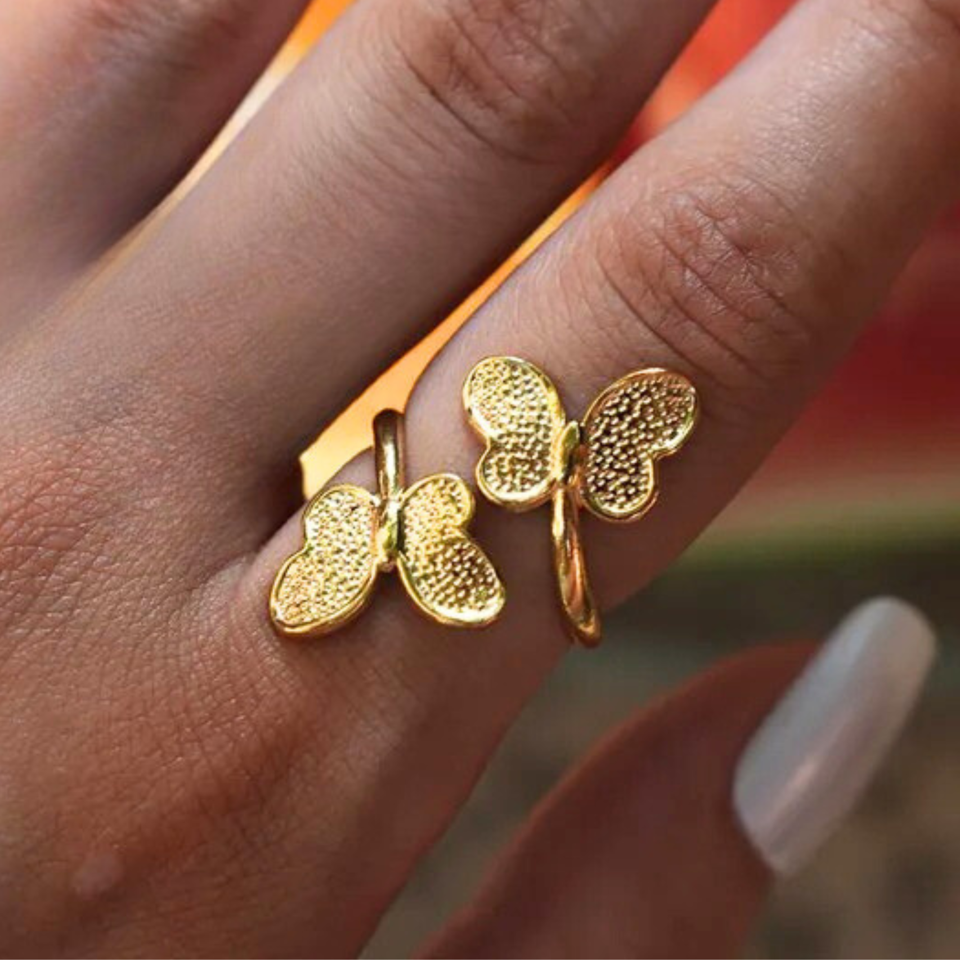 Gold butterfly-shaped ring on a finger with a blurred background