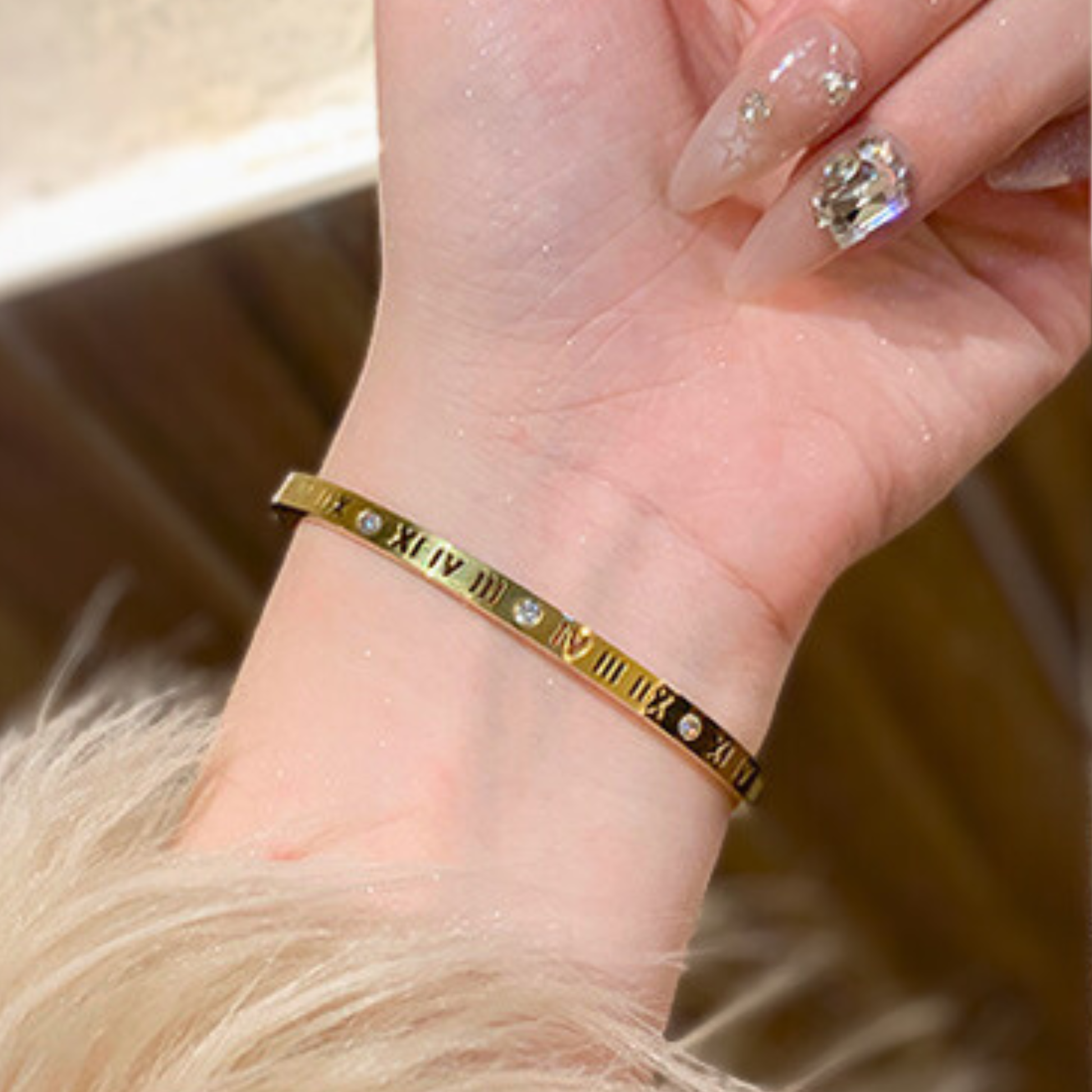 Gold bracelet with Roman numeral design on a wrist, blurred background