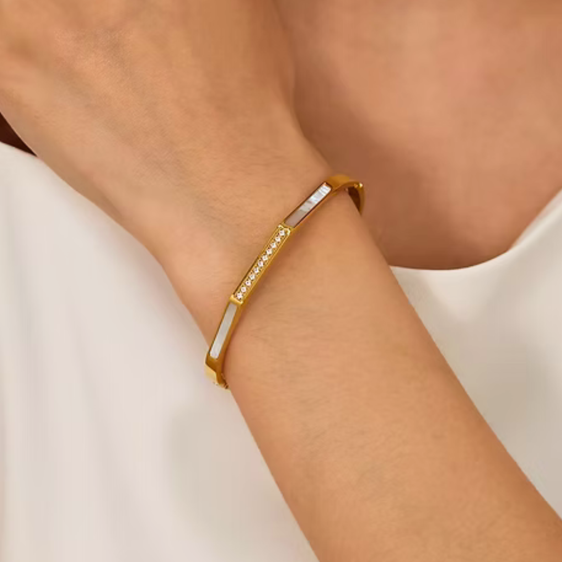 Gold bracelet with embedded stones on a wrist against a neutral background