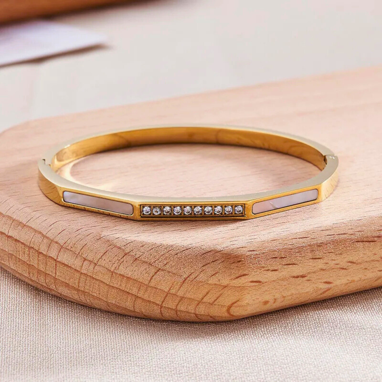 Gold bracelet with embedded stones on a wooden surface