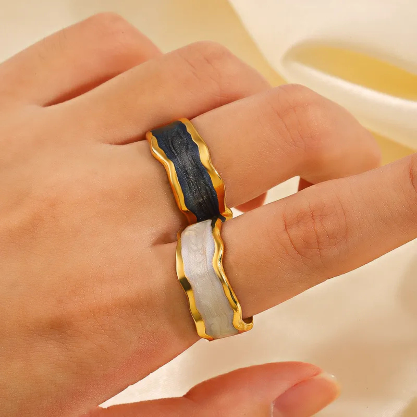 Hand wearing a gold and black ring on a neutral background
