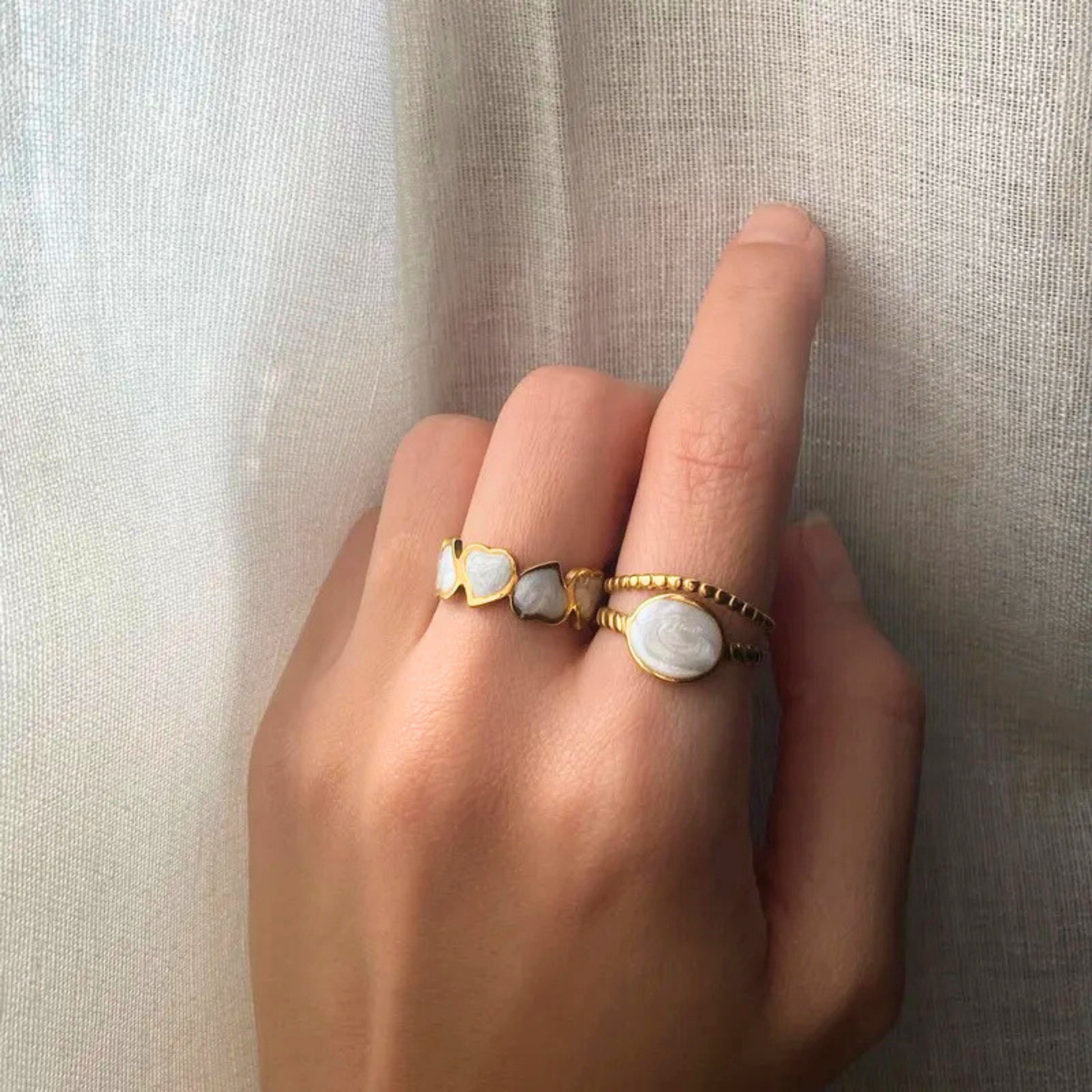 Hand wearing two gold rings with white stones on a neutral background