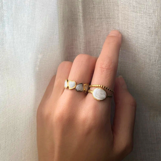 Hand wearing two gold rings with white stones on a neutral background