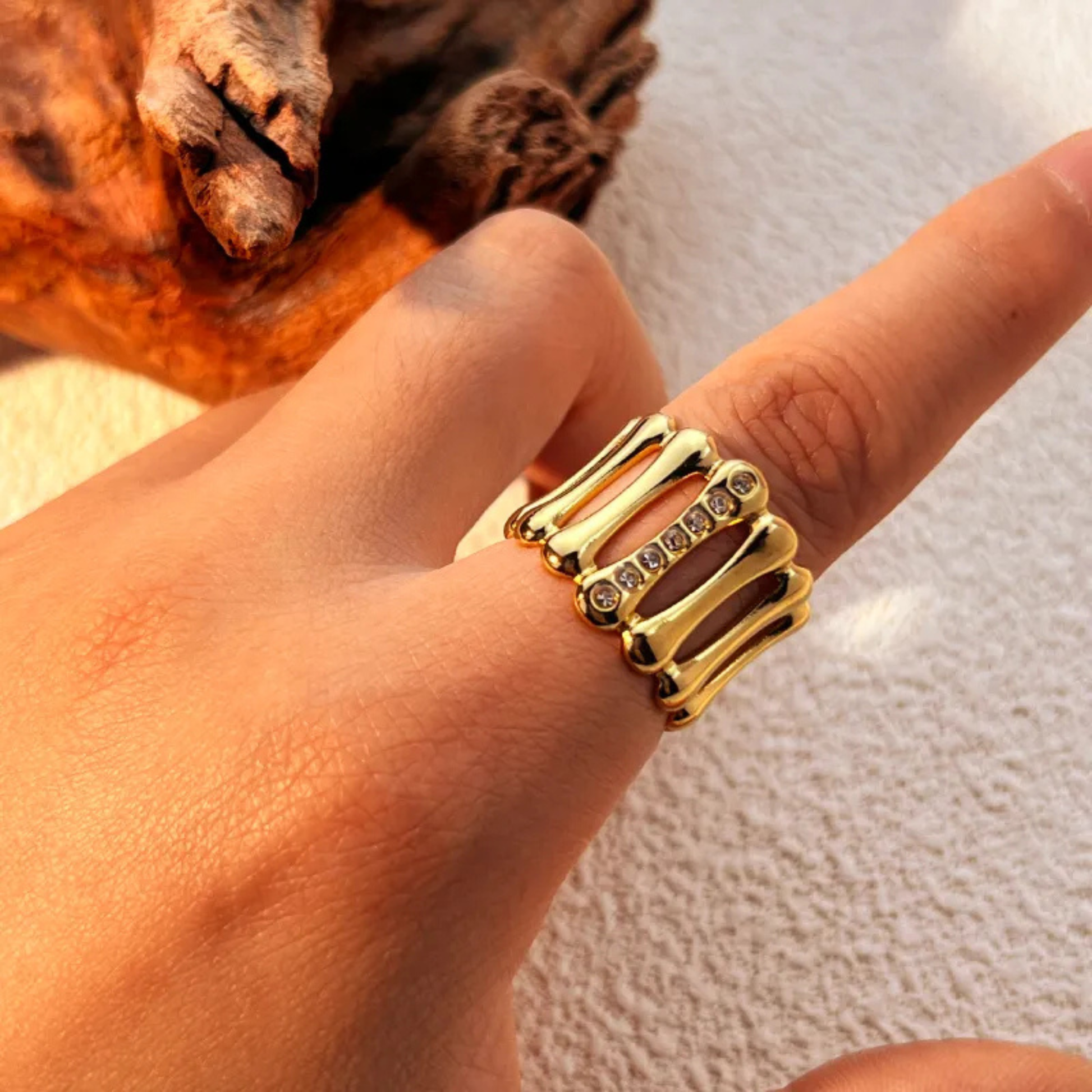 Gold ring with embedded stones on a finger against a neutral background