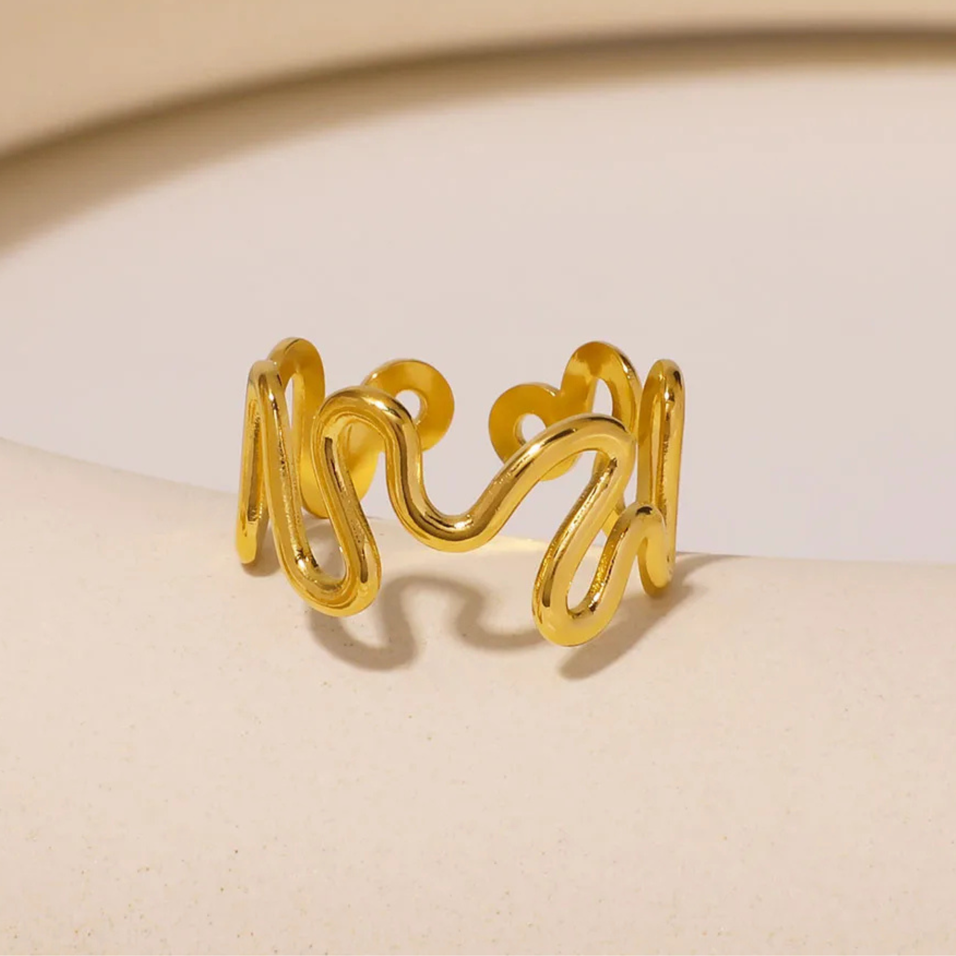Gold ring with wavy design on a beige background