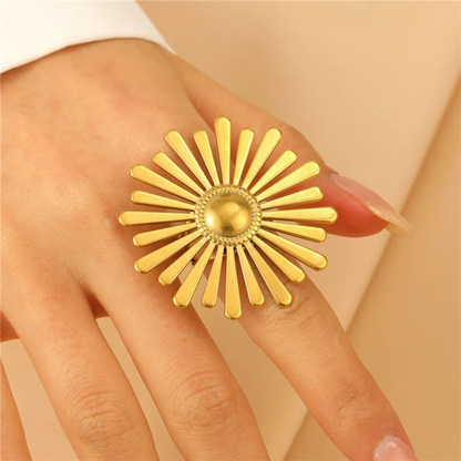 Gold ring with sunburst design on a hand against a beige background