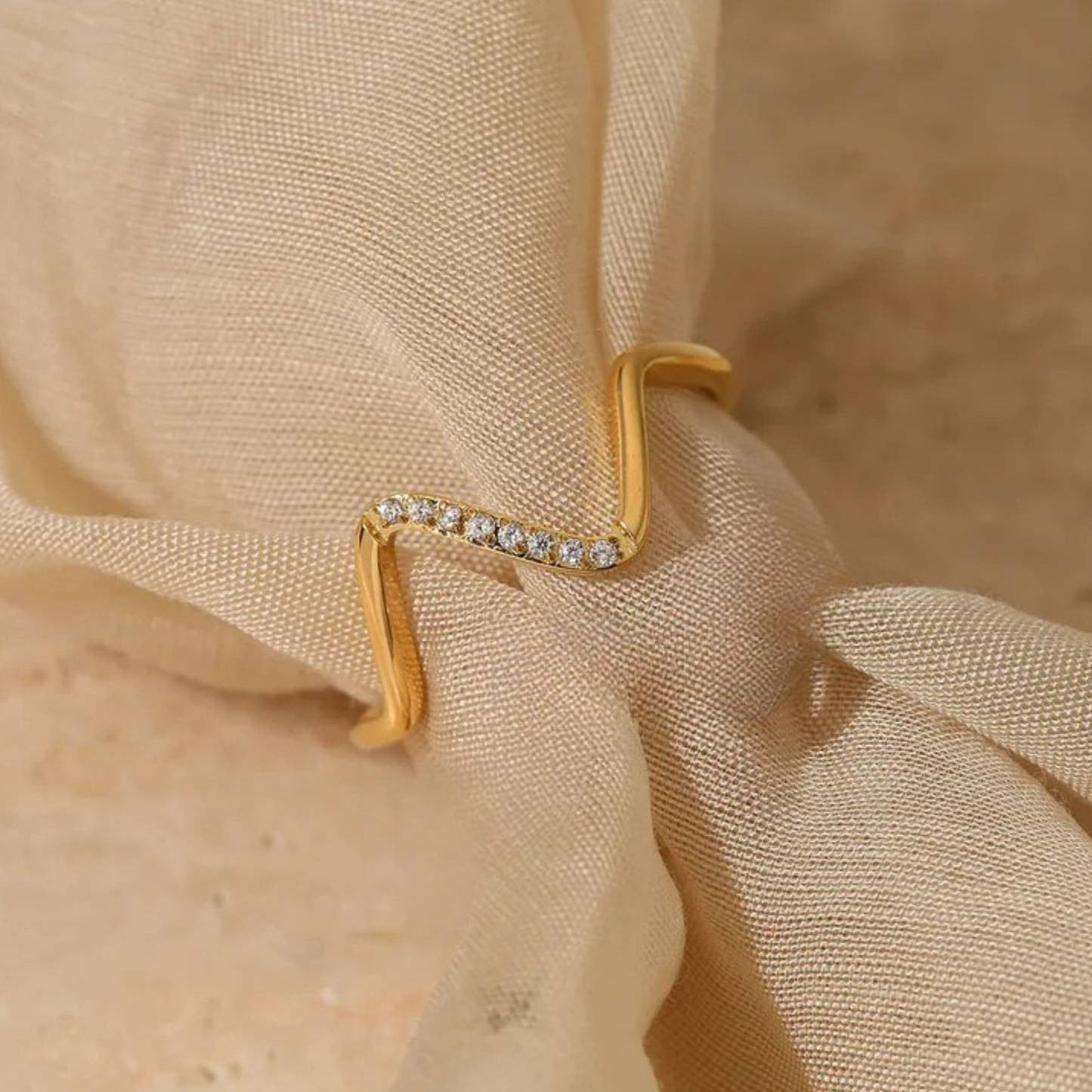 Gold ring with small diamonds on a beige fabric background