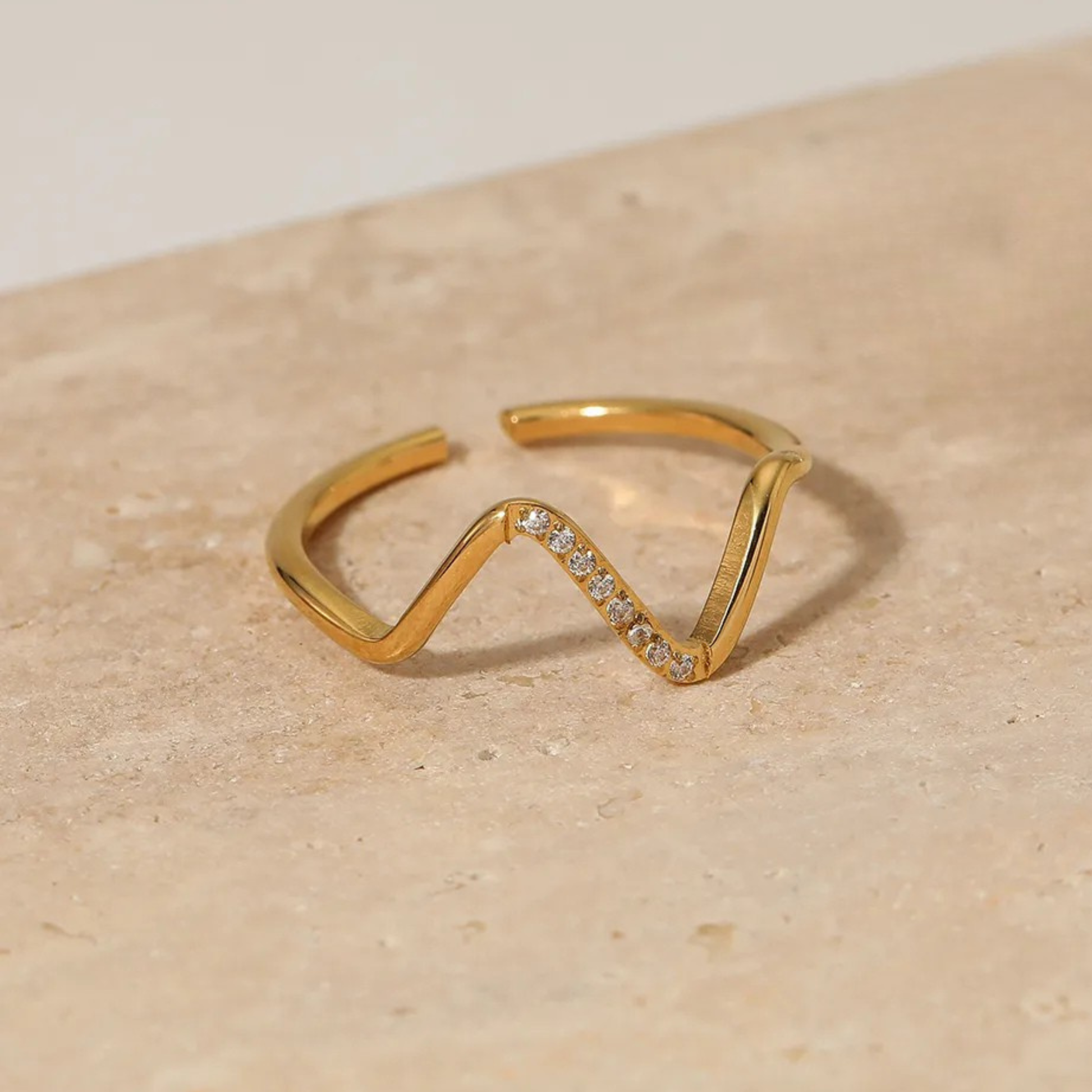 Gold ring with a wavy design and small diamonds on a beige surface