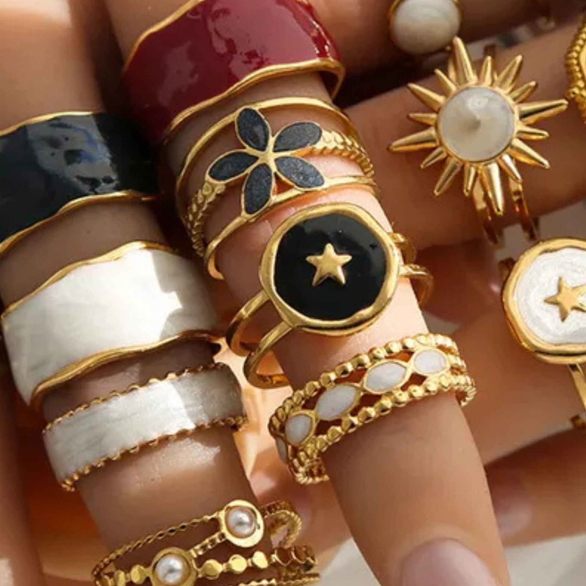 Collection of gold and black rings on a hand against a neutral background