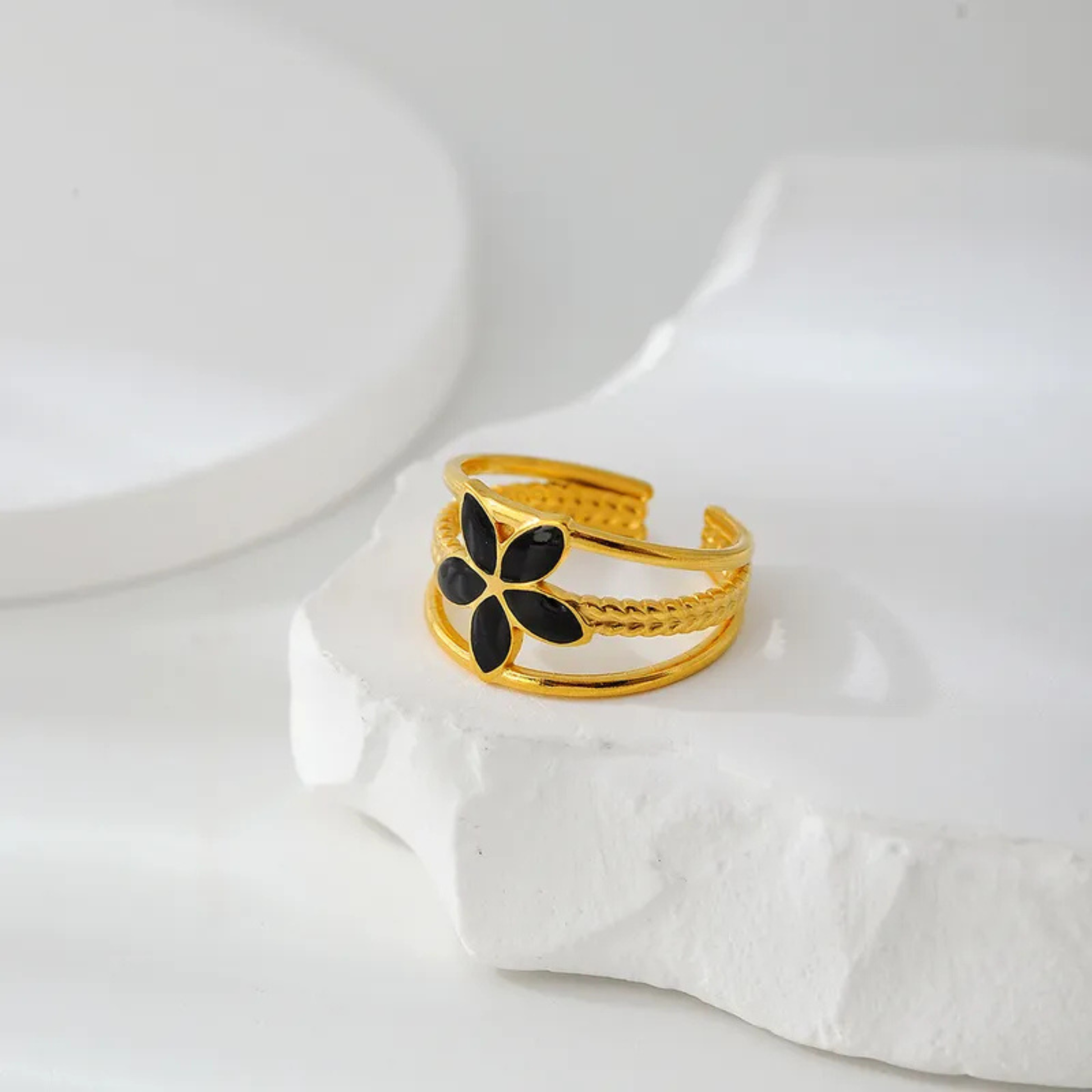 Gold ring with a black flower design on a white surface