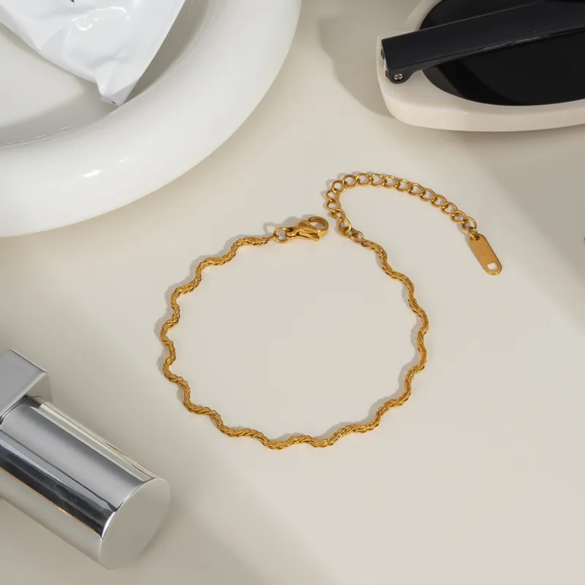Gold bracelet on a white surface with a teapot and kettle in the background