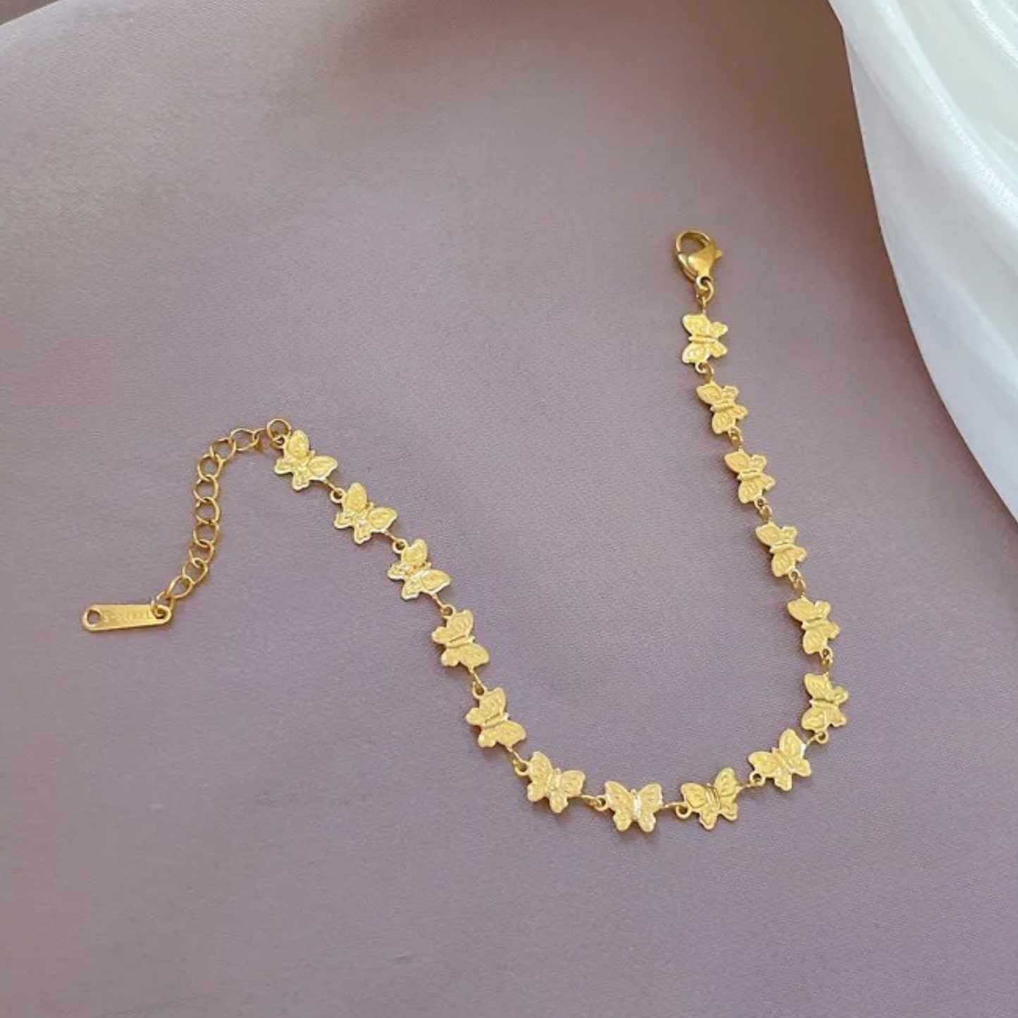 Gold butterfly bracelet on a person's wrist against a neutral background