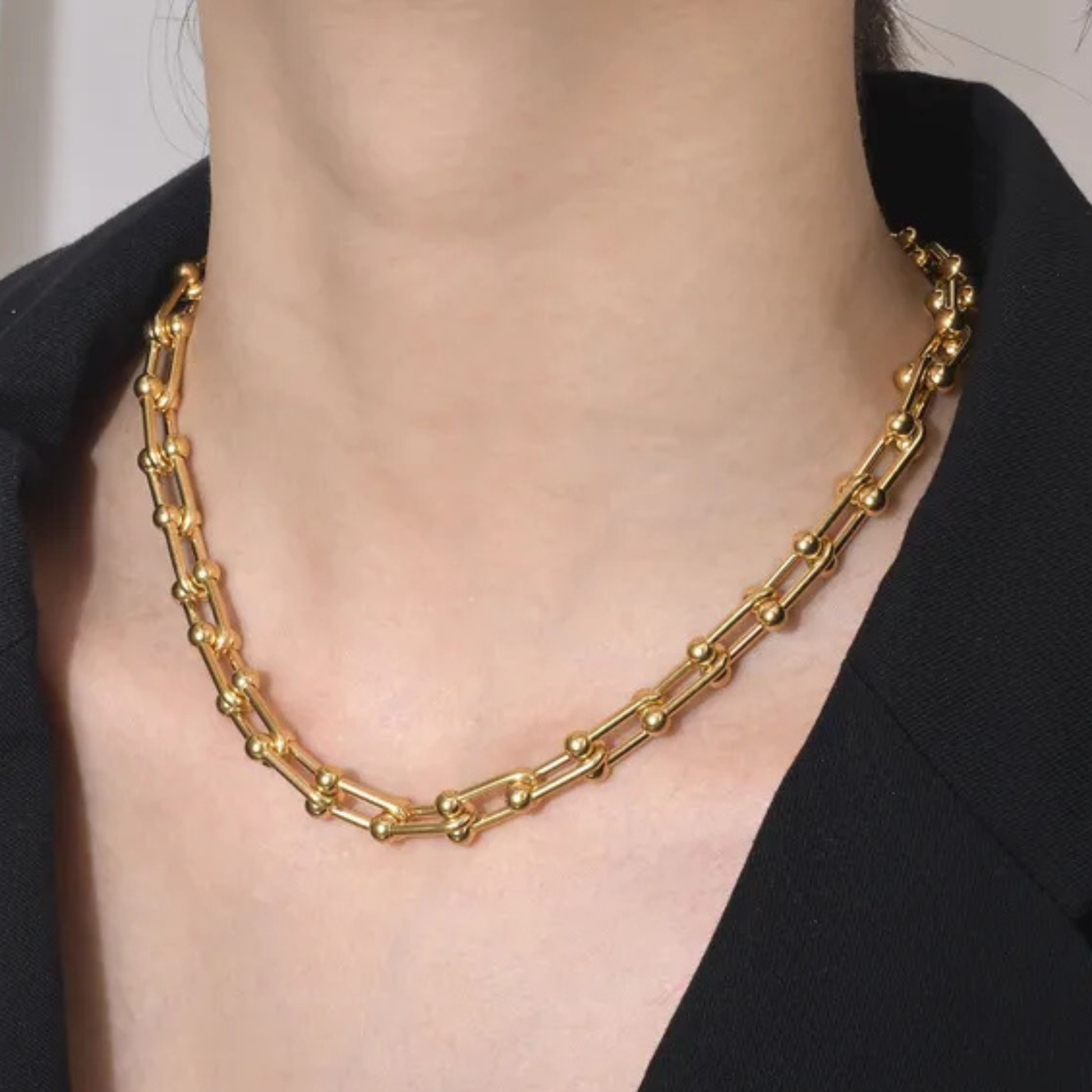 Gold chain necklace worn by a person with a black background