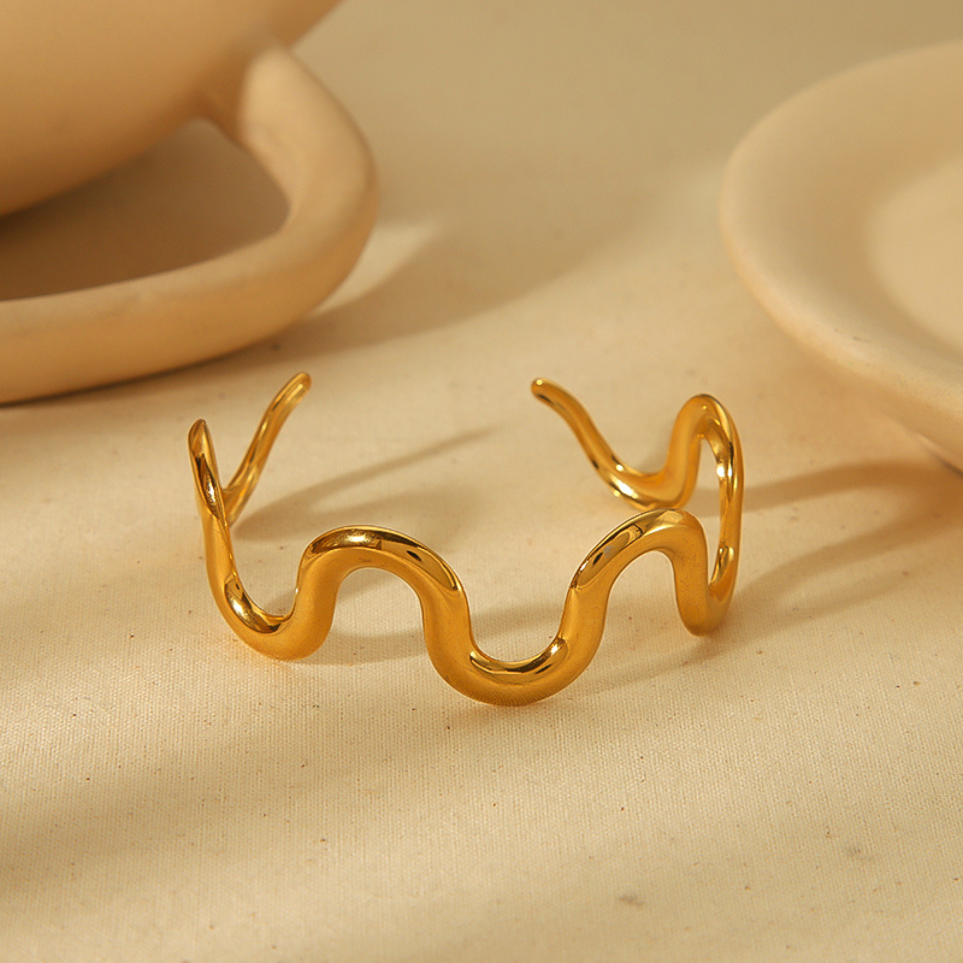 Gold wavy bracelet on a beige fabric background