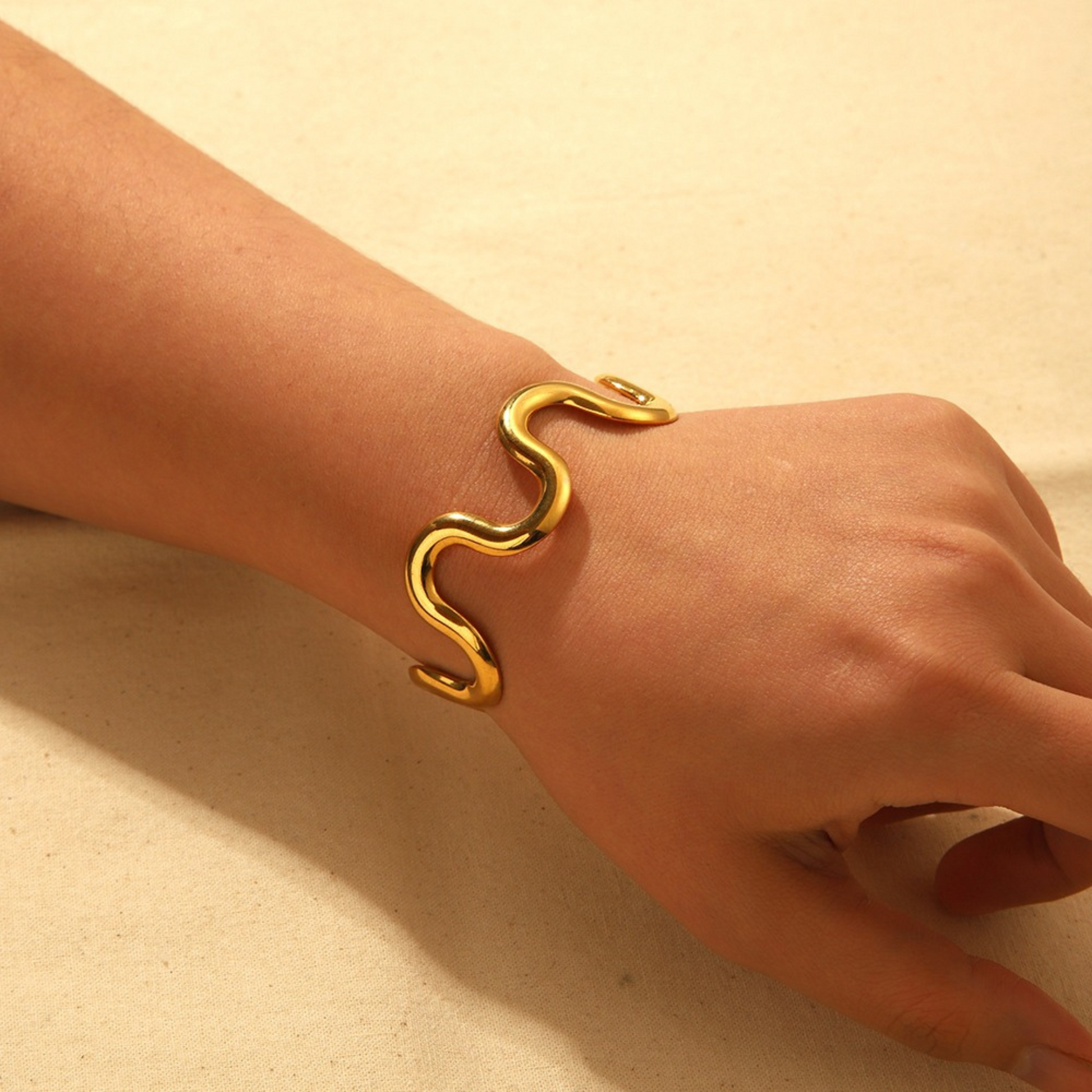 Gold bracelet on a wrist against a beige background