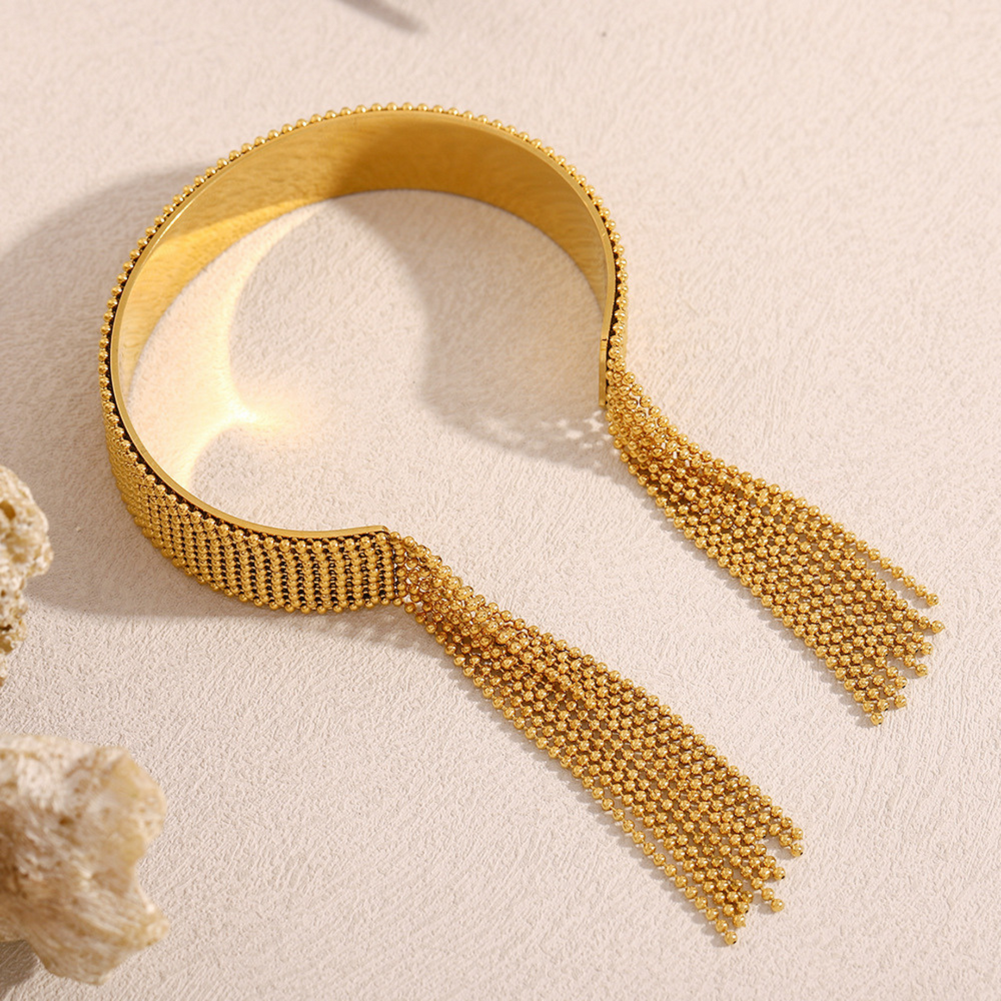 Gold bracelet with tassels on a beige background