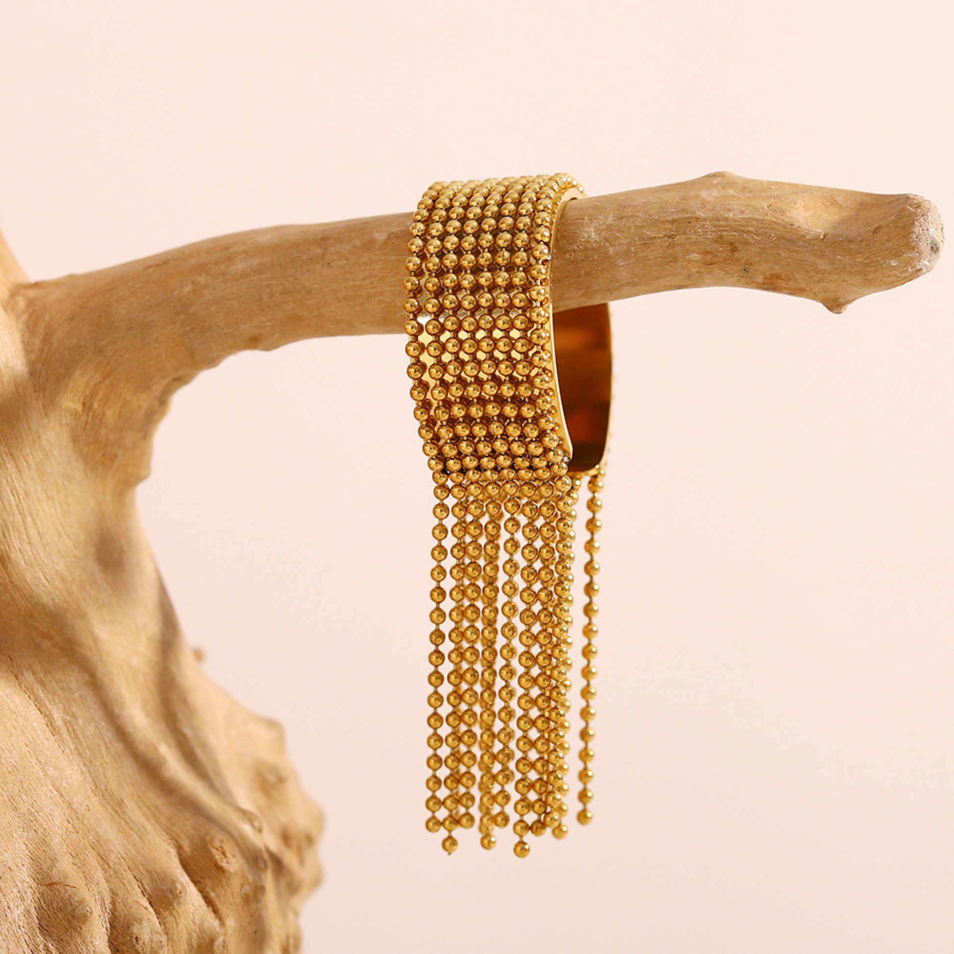 Gold bracelet with dangling beads on a wooden branch against a beige background