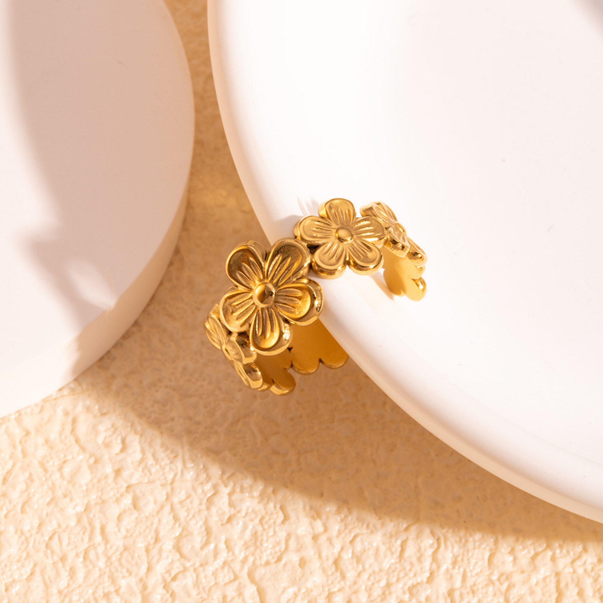 Gold floral ring on a textured beige surface with a white background
