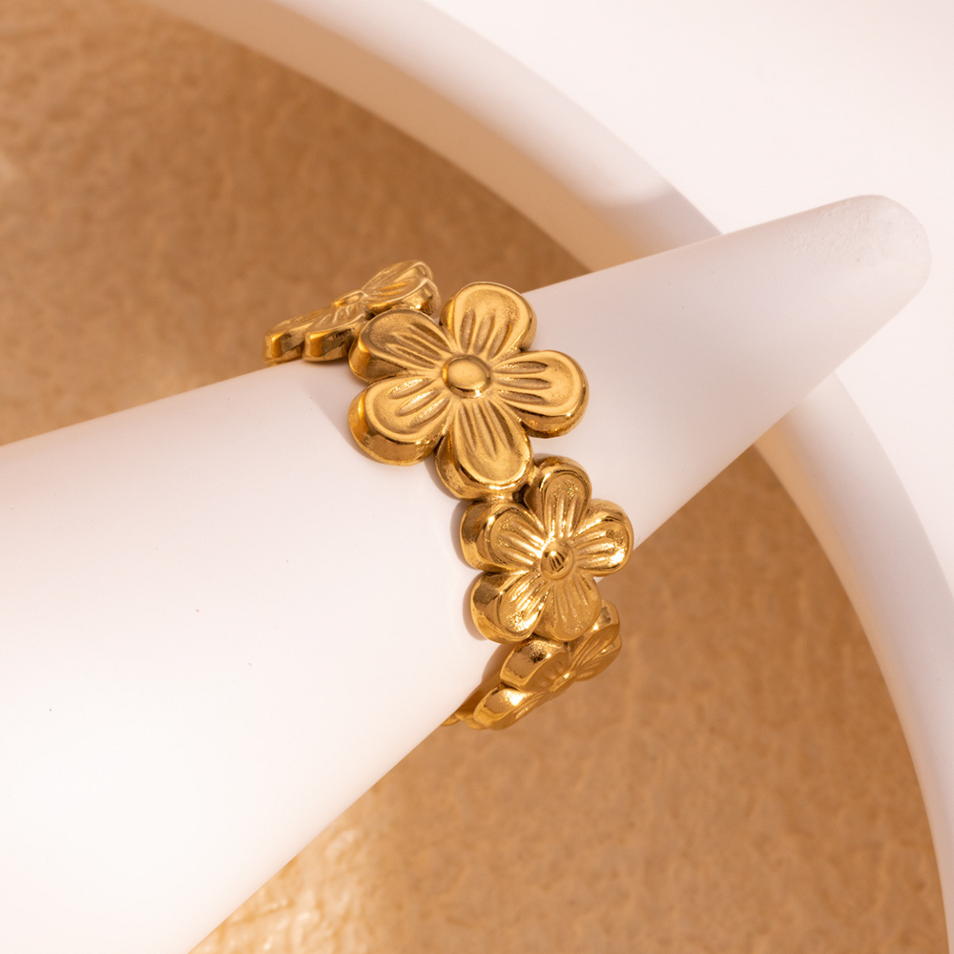 Gold bracelet with floral designs on a white stand against a beige background