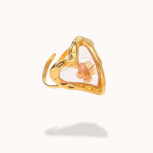Gold ring with a clear heart-shaped stone featuring a small orange flower on a white background