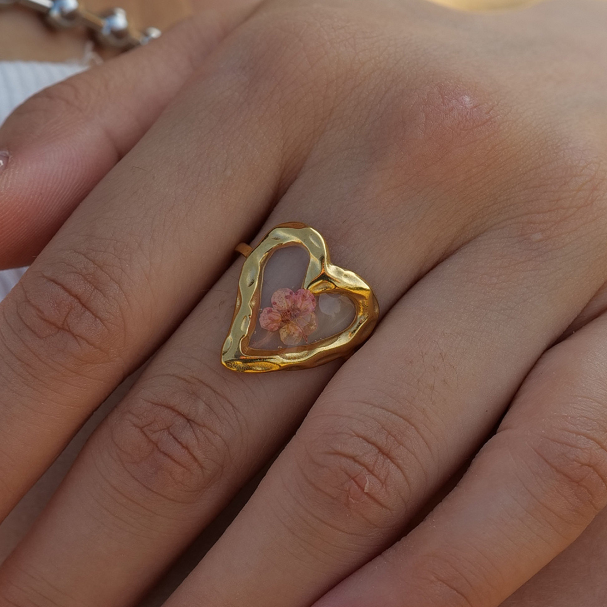 Gold heart-shaped ring with a floral design on a person's finger