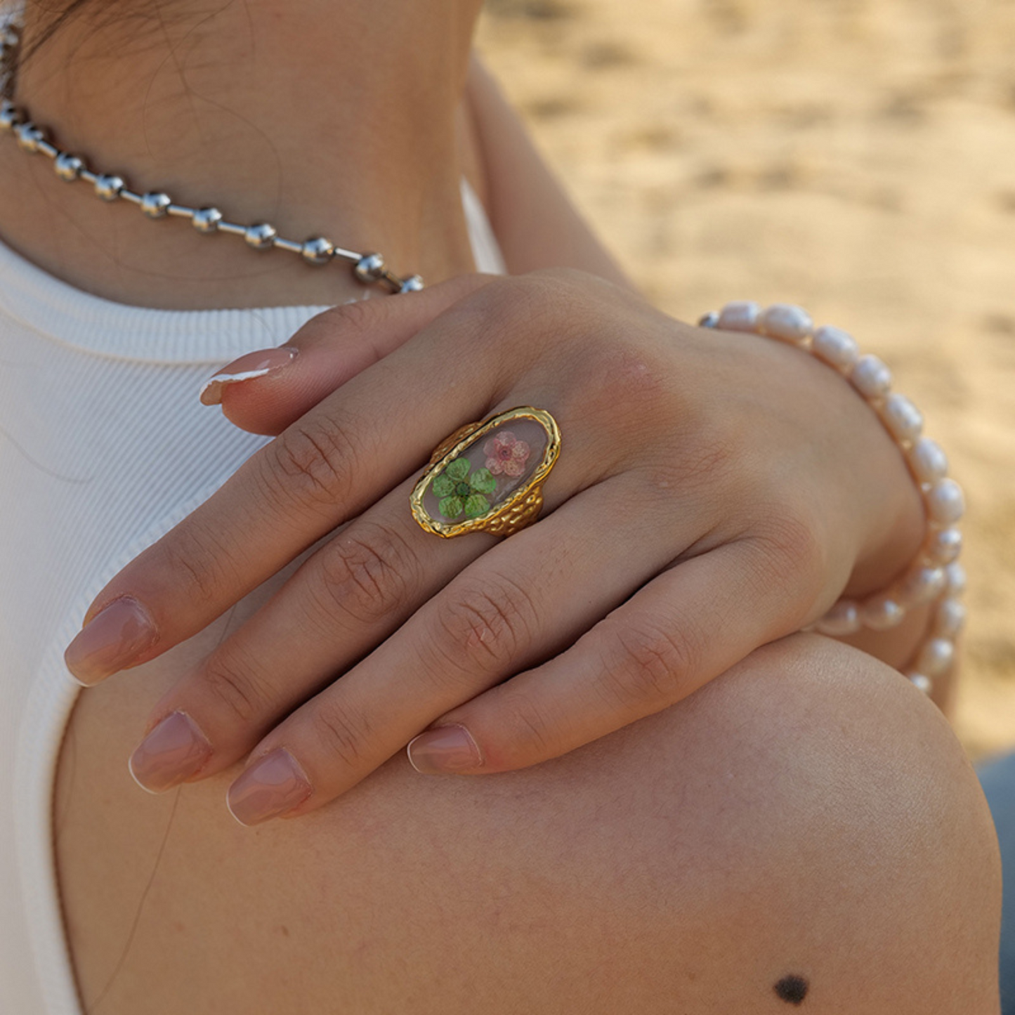 Close-up of a hand wearing a gold ring with a green stone, pearl bracelet, and silver necklace.